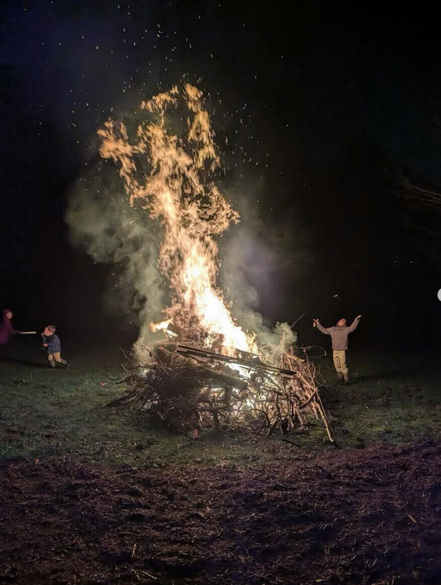 A large bonfire at night with figures silhouetted against the flames.