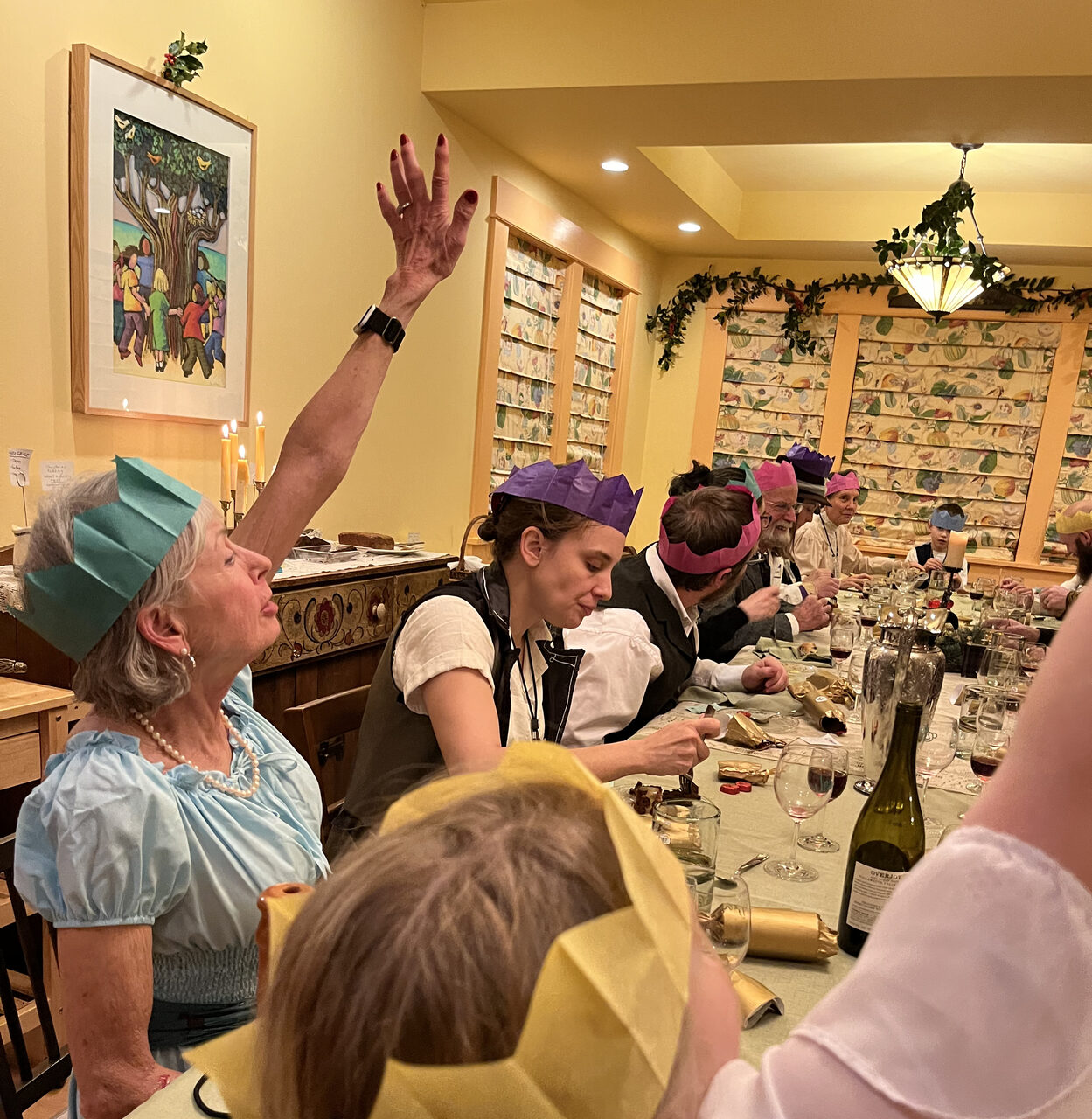 A long table in the Common House set for a holiday dinner, diners in paper crowns, candles and greenery around the room.